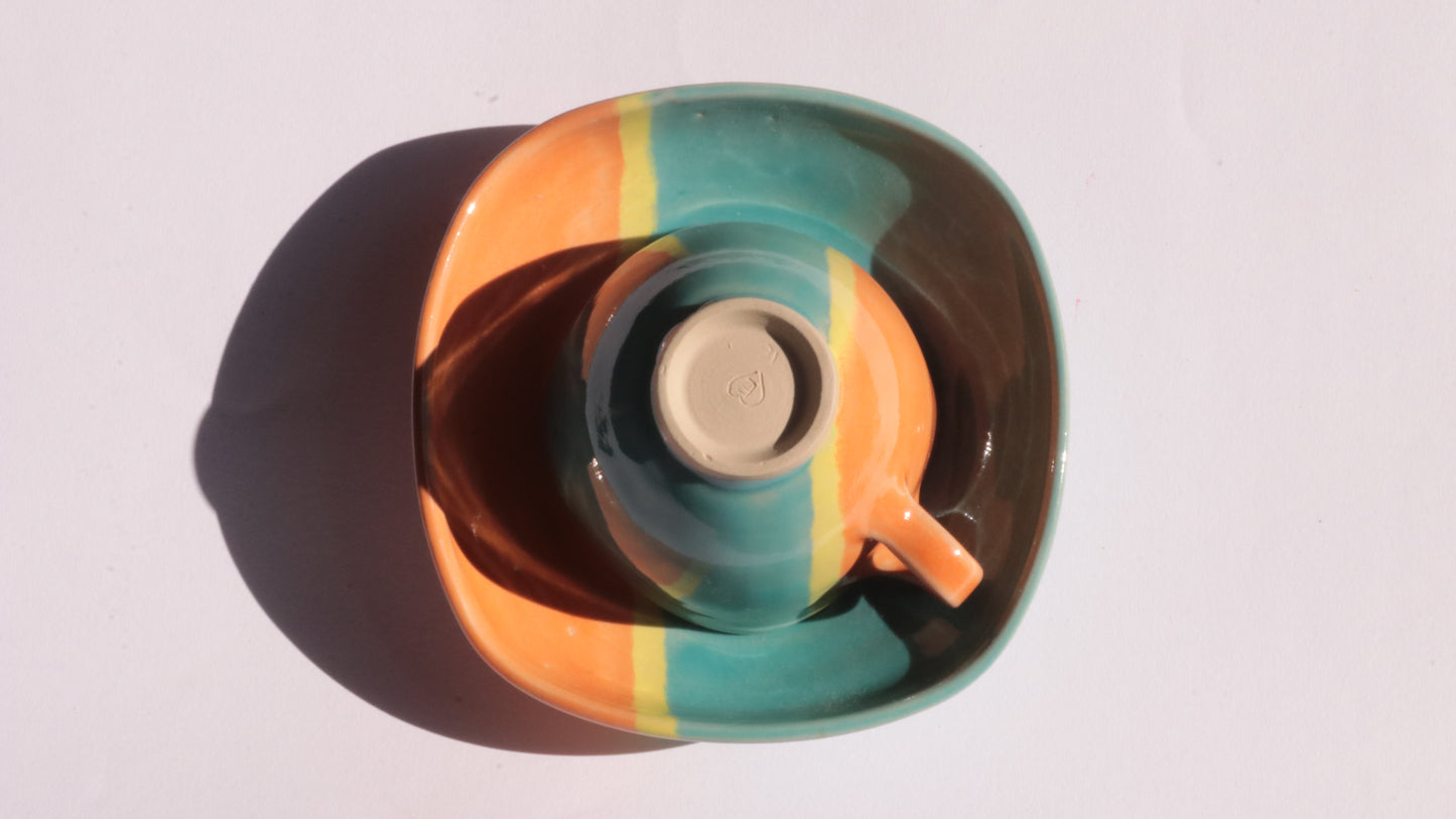 Teal and orange ceramic cup and saucer with yellow stripe on a white background