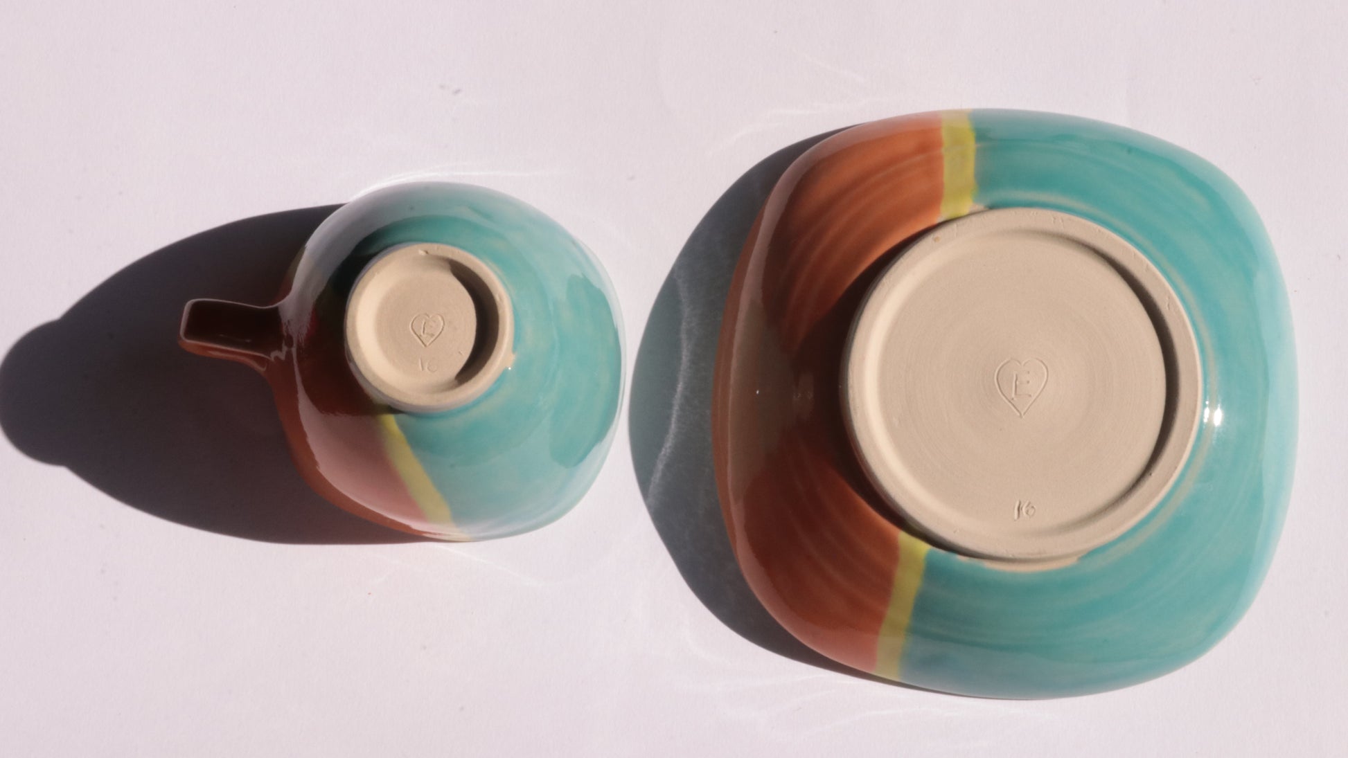 Teal and orange ceramic cup and saucer with yellow stripe on a white background