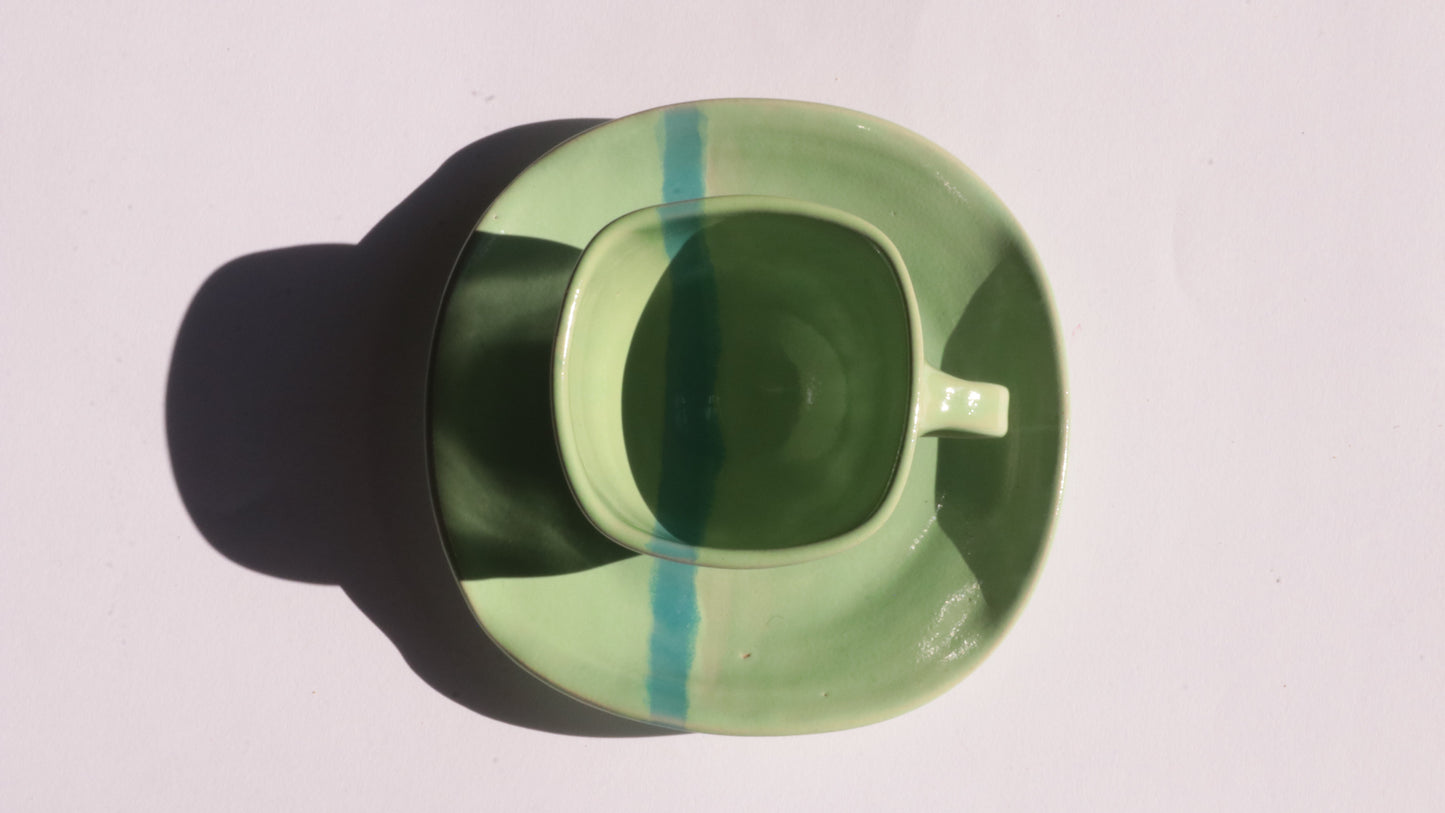 green ceramic cup and saucer with blue stripe on white background