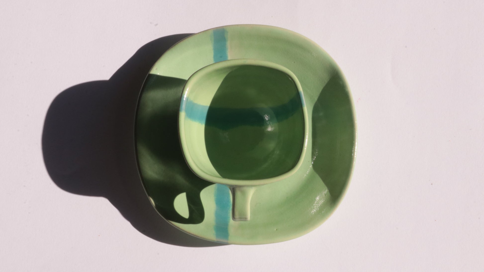 green ceramic cup and saucer with blue stripe on white background