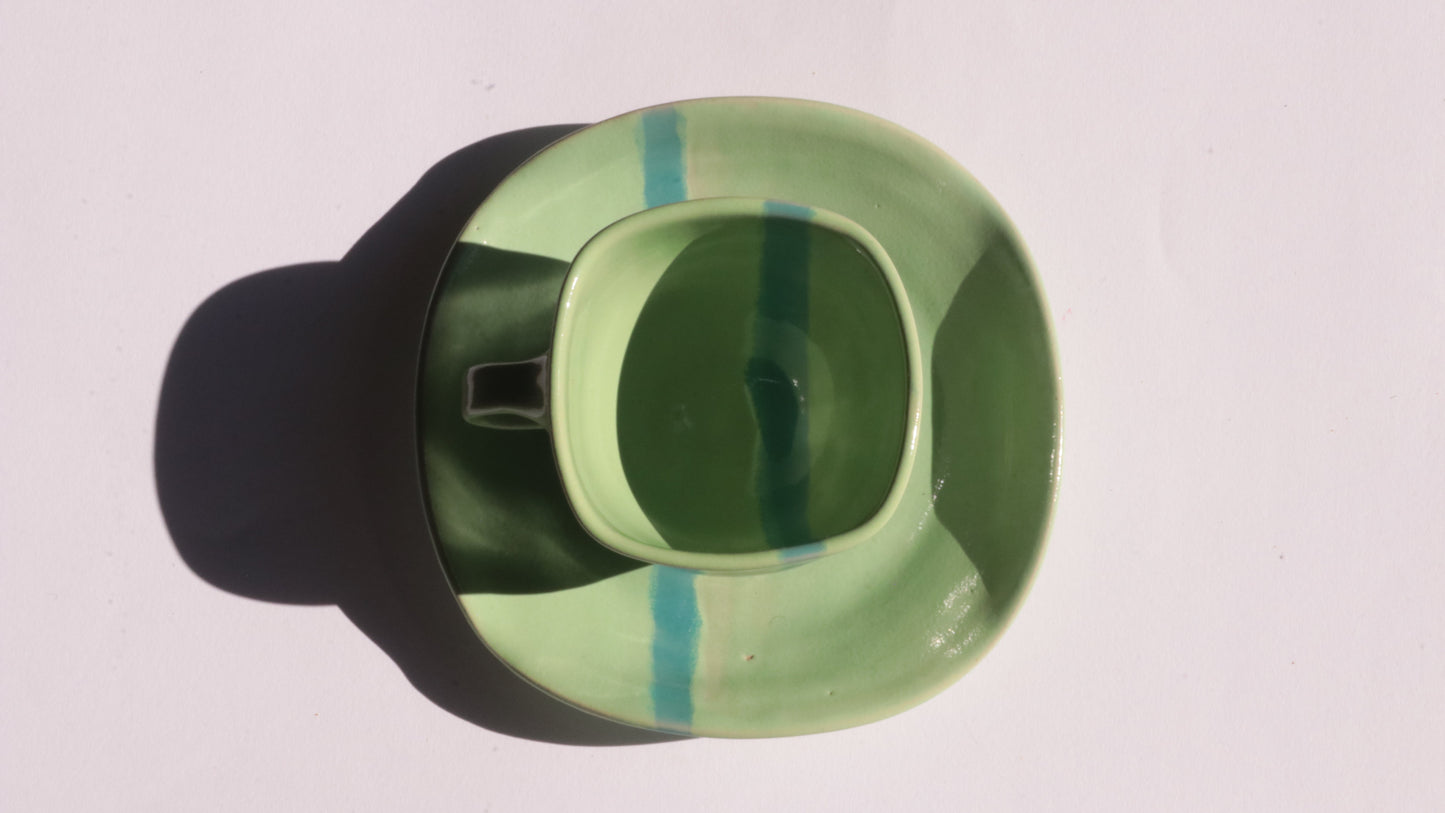 green ceramic cup and saucer with blue stripe on white background