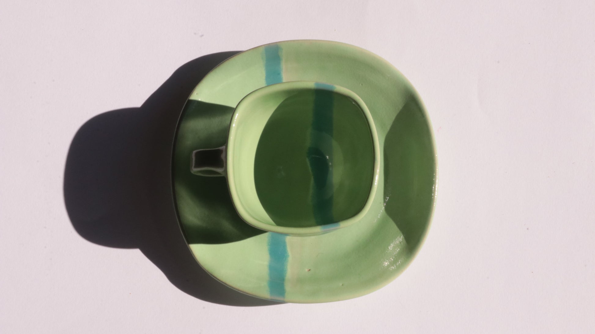 green ceramic cup and saucer with blue stripe on white background