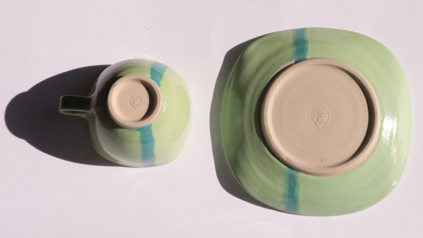 green ceramic cup and saucer with blue stripe on white background
