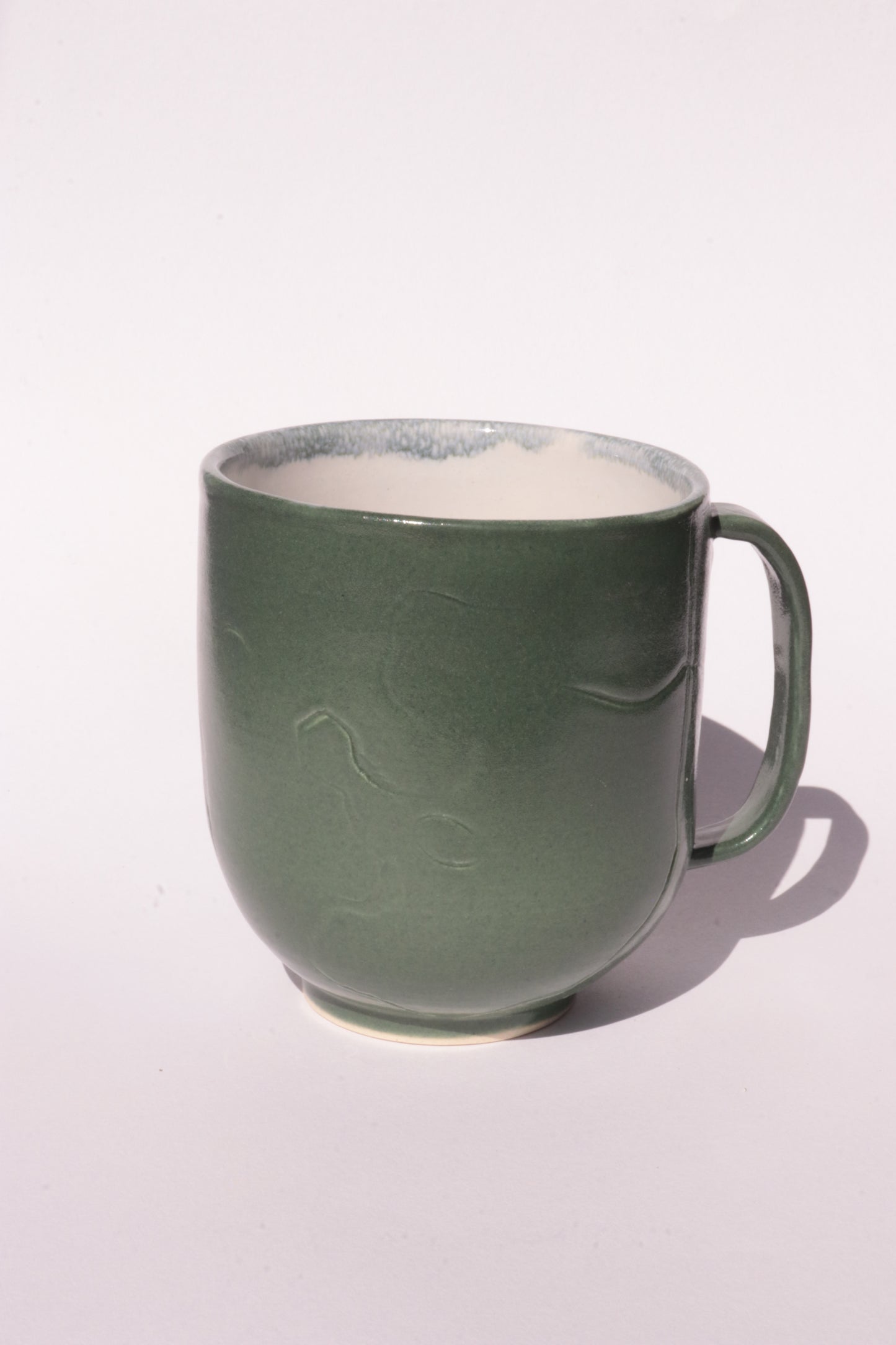 Dark green mug with engraved abstract design on a white background
