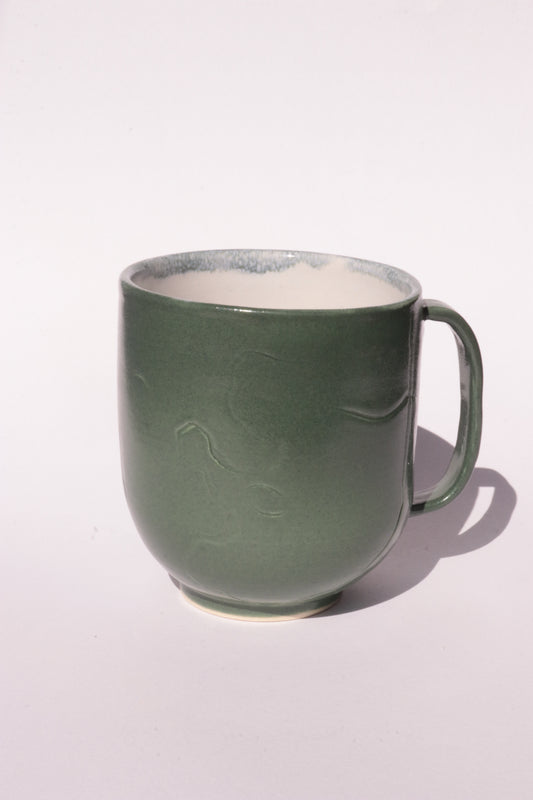 Dark green mug with engraved abstract design on a white background
