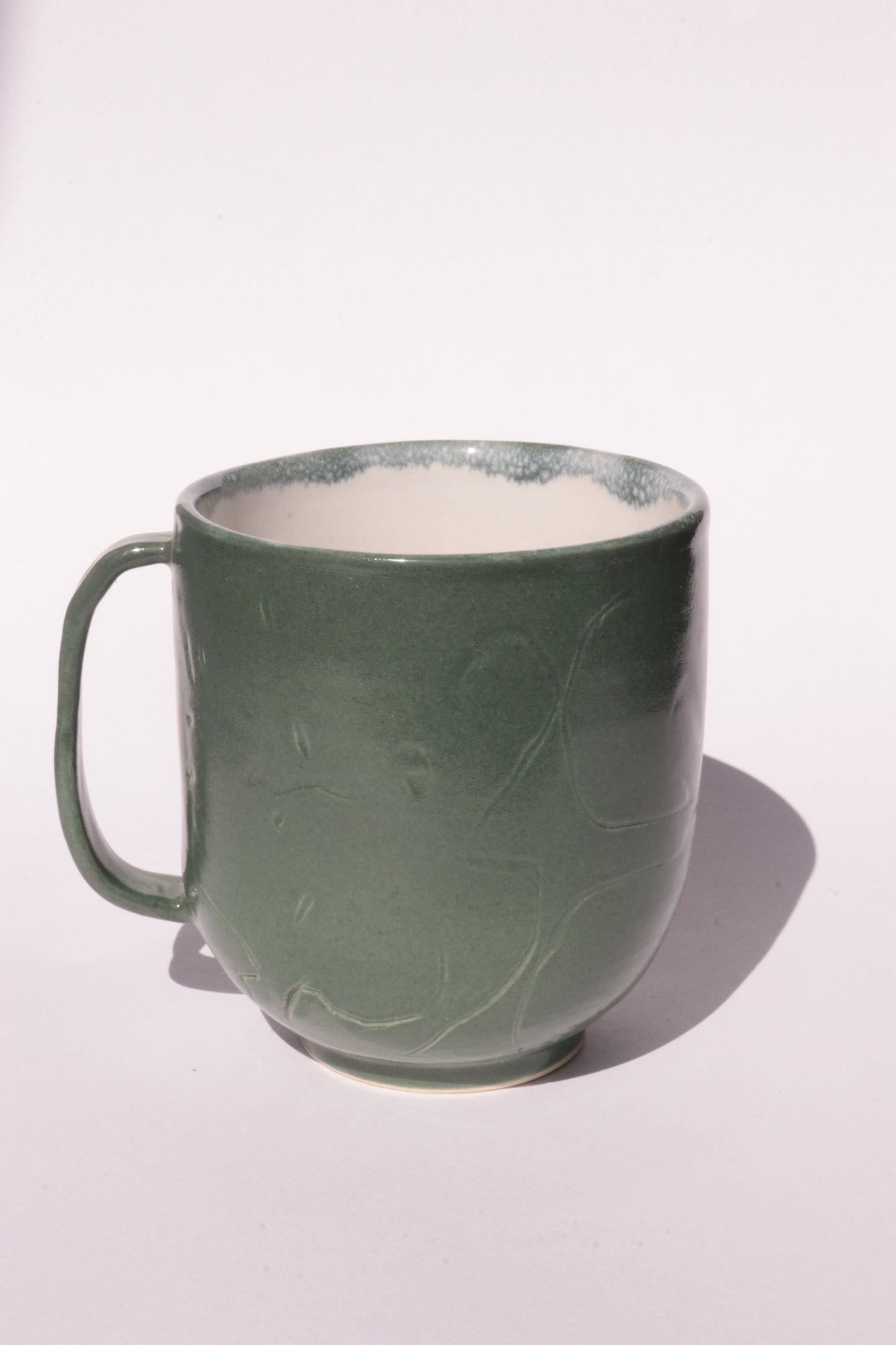 Dark green mug with engraved abstract design on a white background