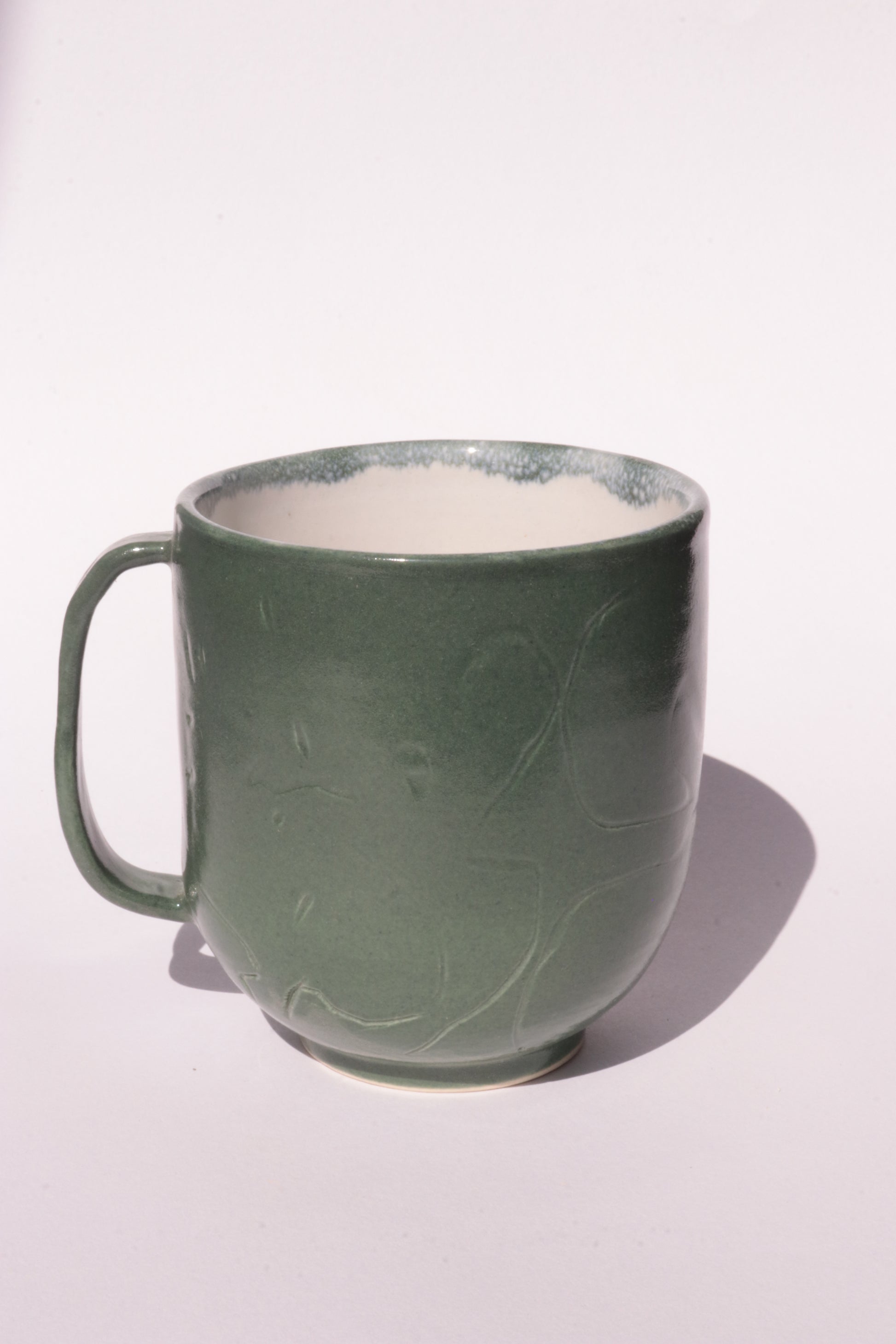 Dark green mug with engraved abstract design on a white background