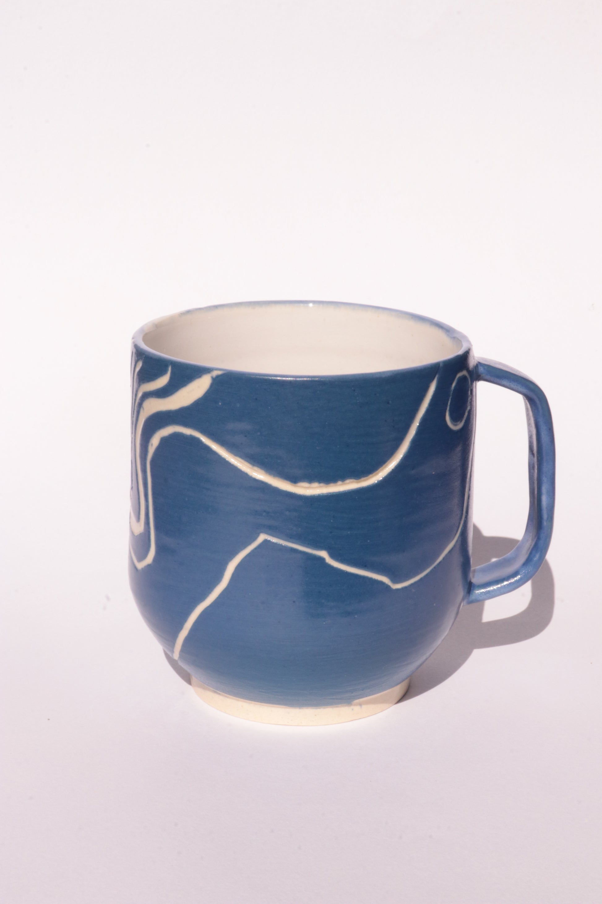 Blue mug with engraved white abstract design on a white background