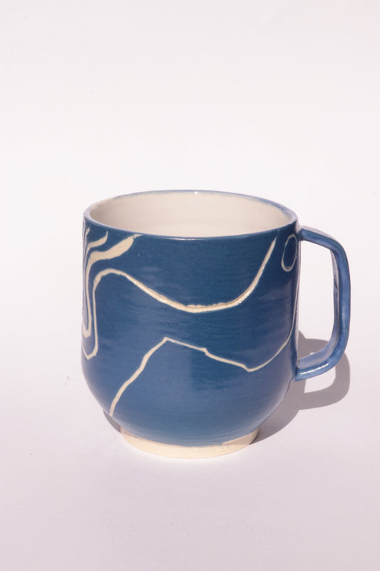 Blue mug with engraved white abstract design on a white background
