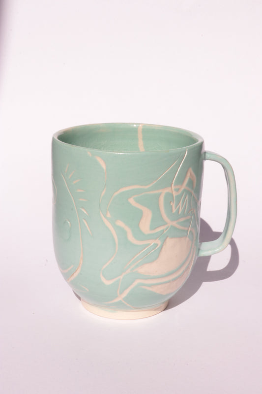Teal mug with engraved white abstract design on a white background