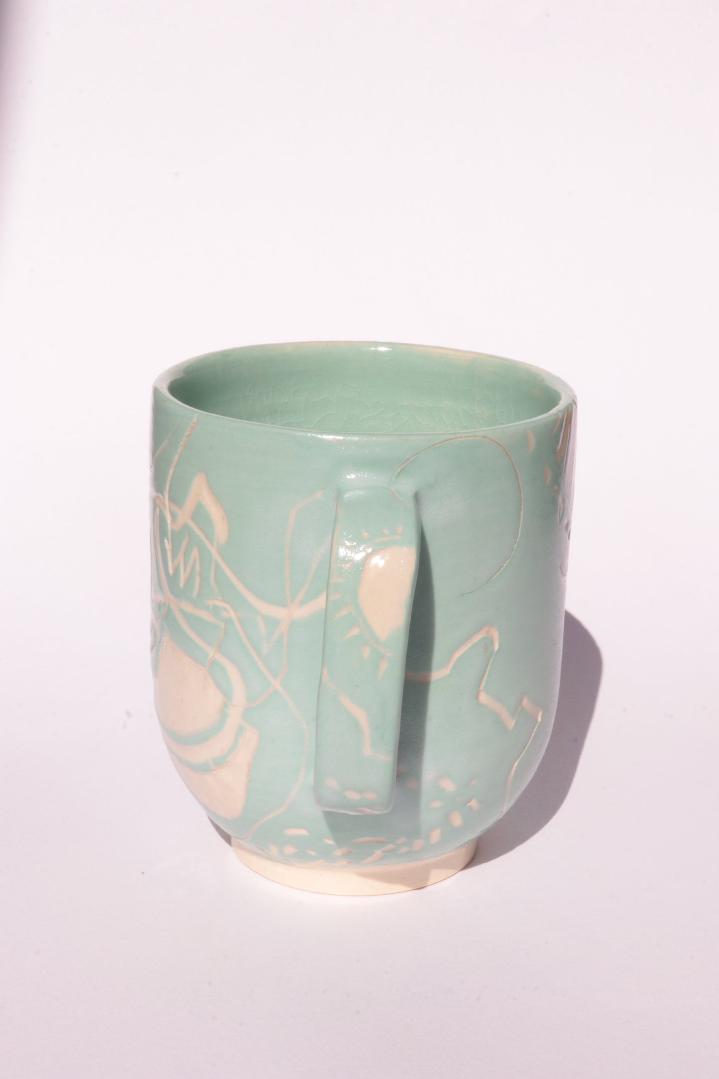 Teal mug with engraved white abstract design on a white background
