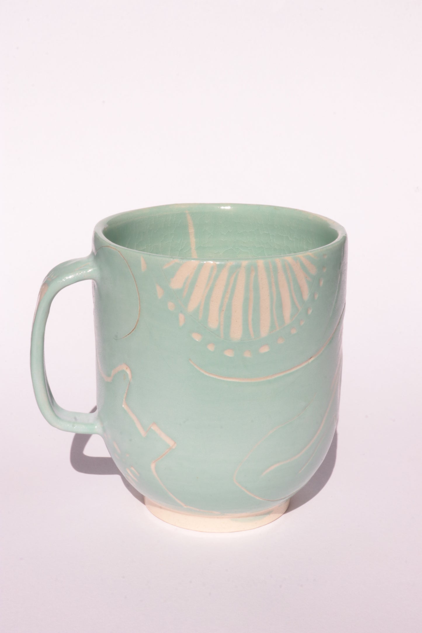 Teal mug with engraved white abstract design on a white background