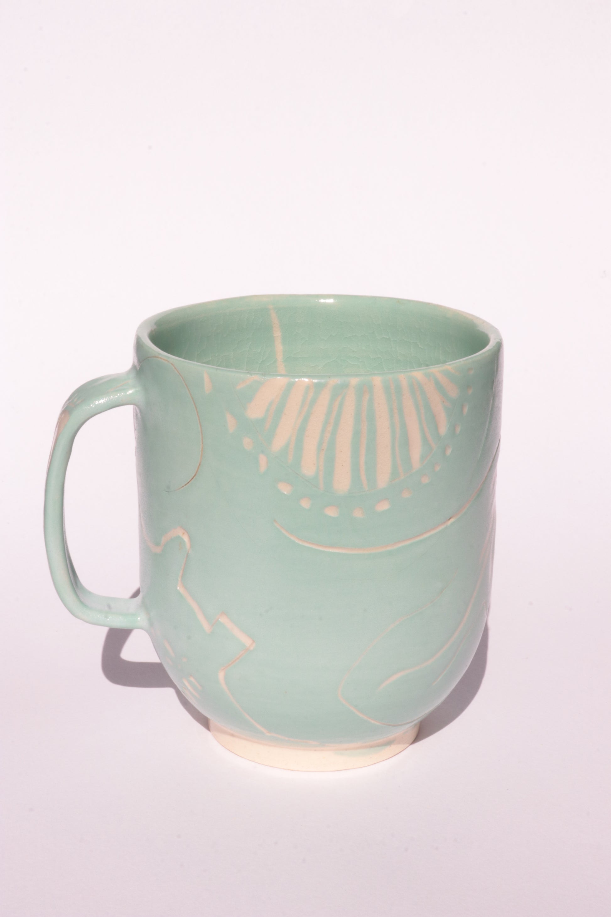 Teal mug with engraved white abstract design on a white background