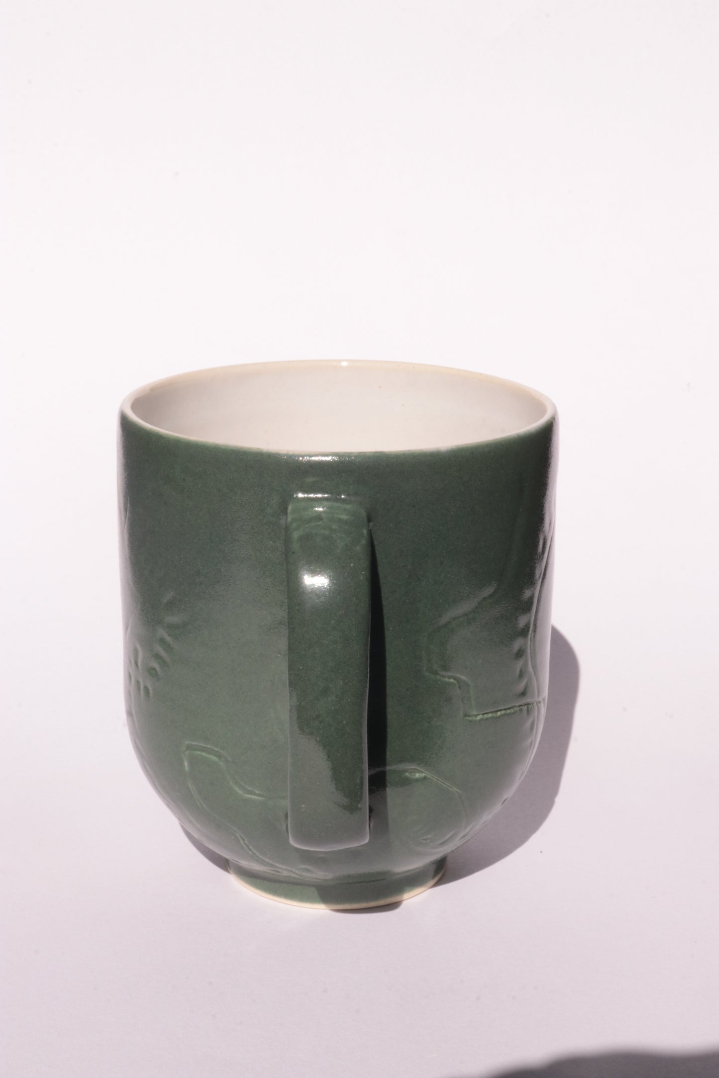Dark green mug with subtle engraved design on a white background