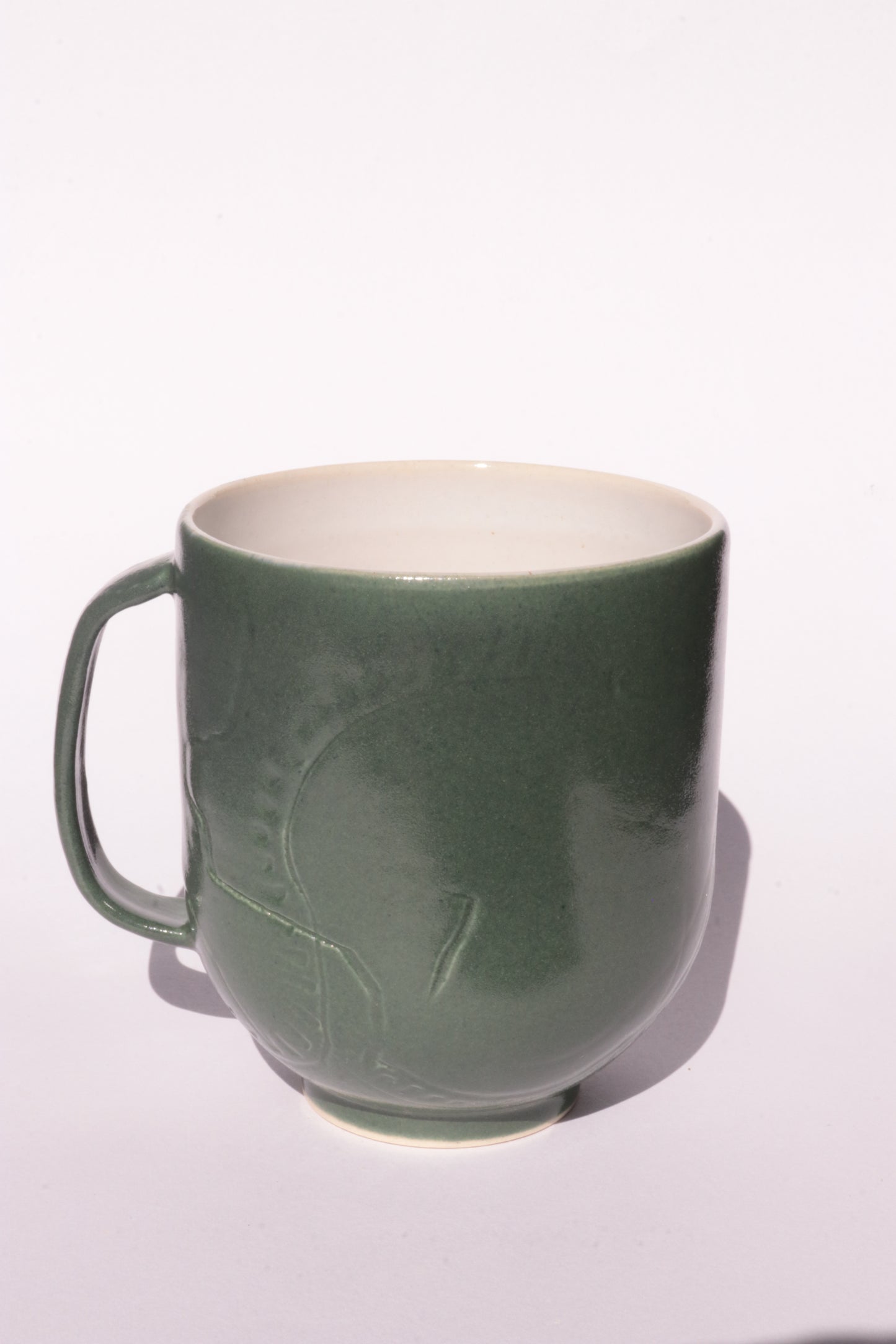 Dark green mug with subtle engraved design on a white background