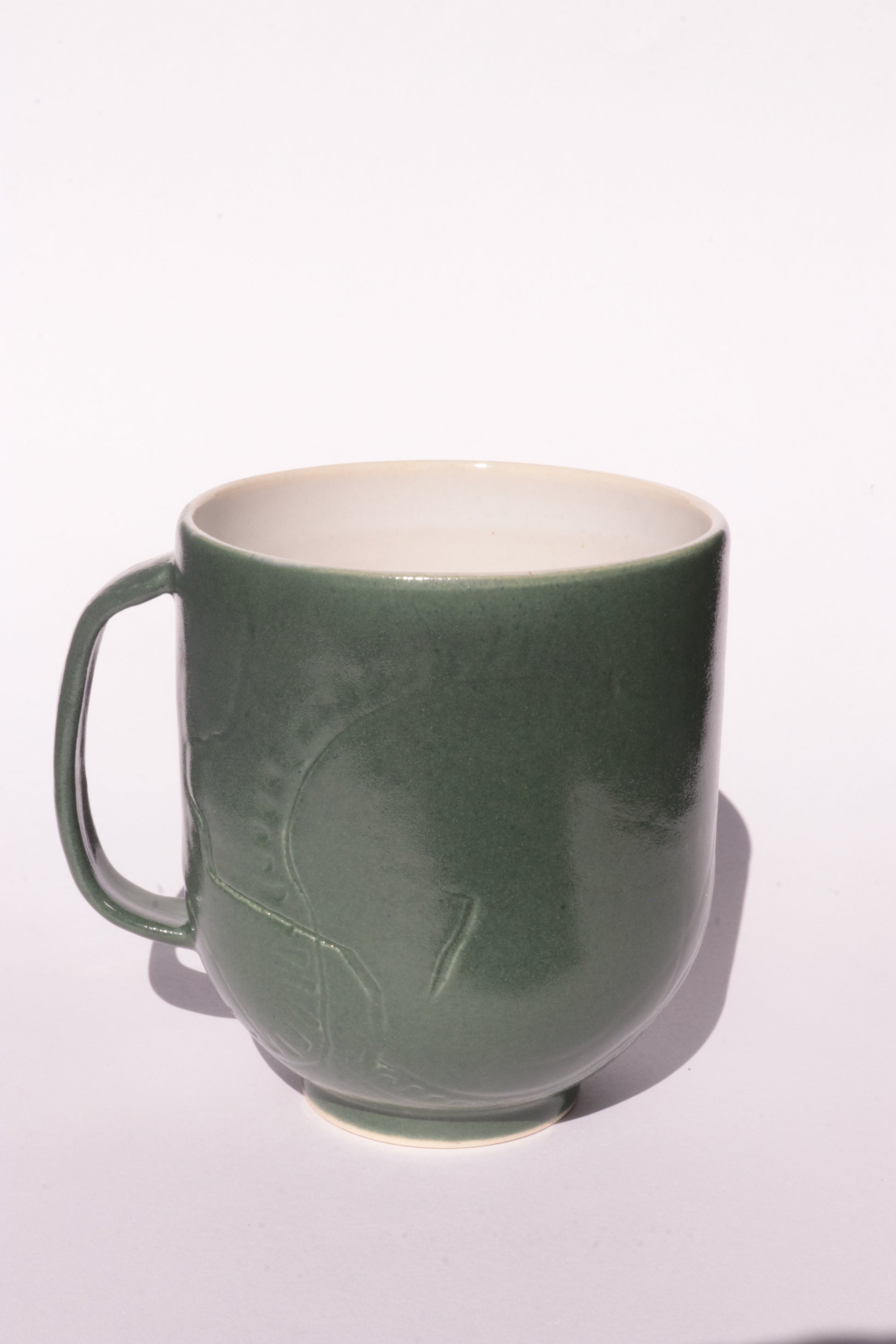 Dark green mug with subtle engraved design on a white background