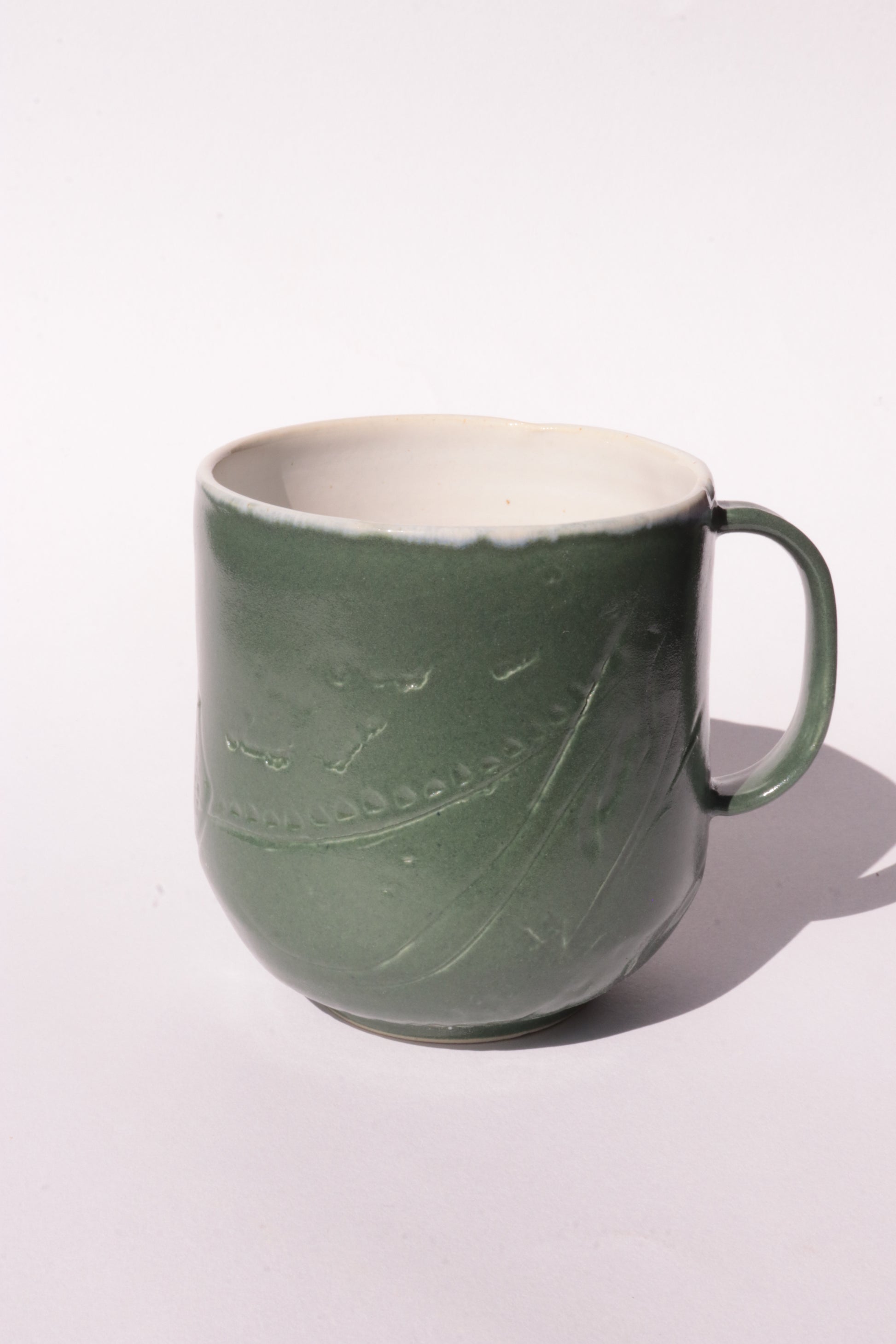 Dark green mug with subtle engraved design on a white background