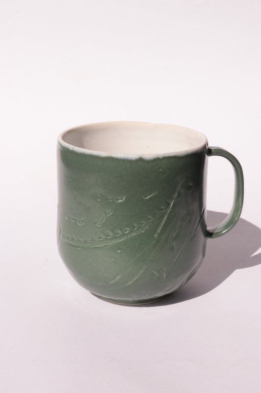 Dark green mug with subtle engraved design on a white background