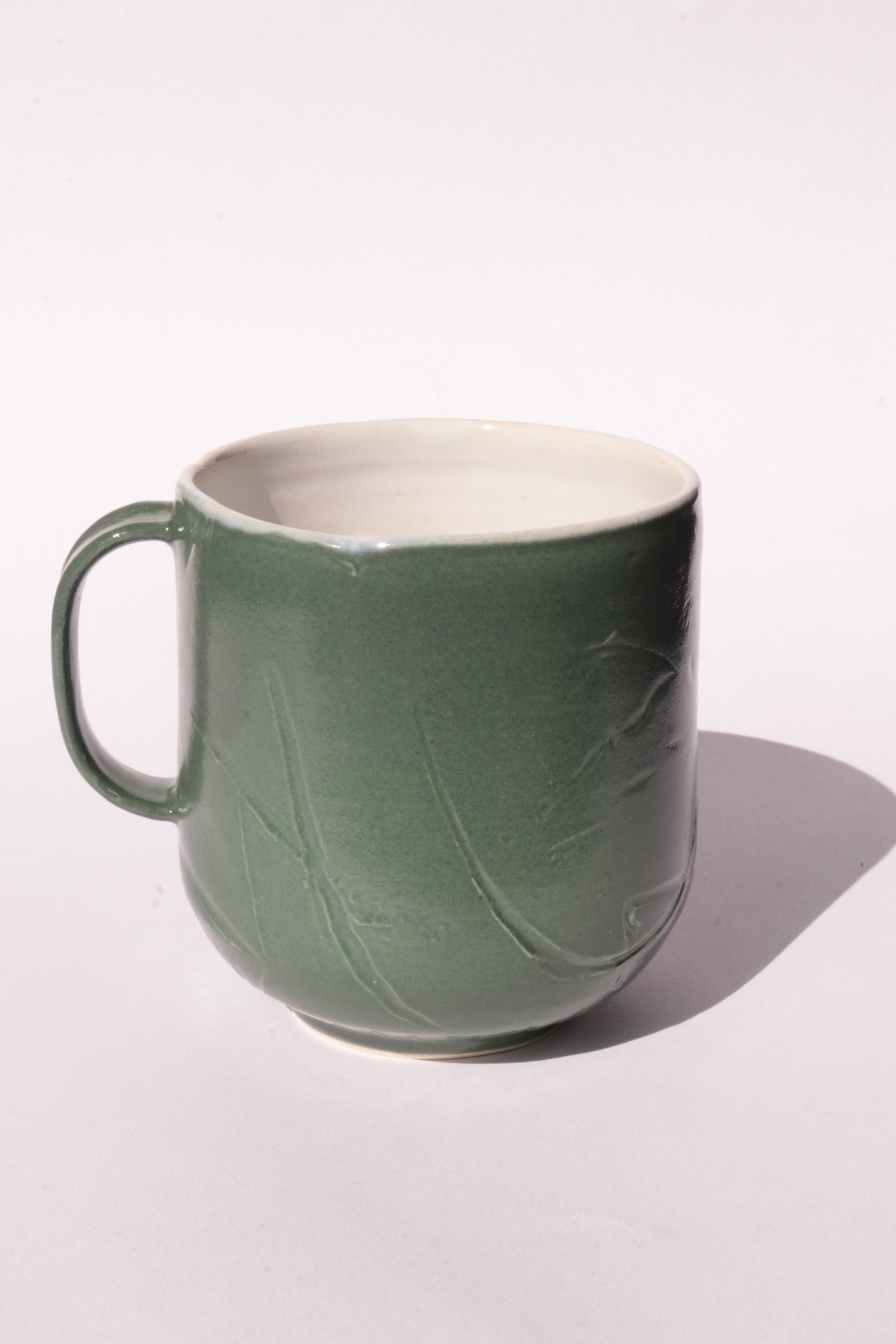 Dark green mug with subtle engraved design on a white background