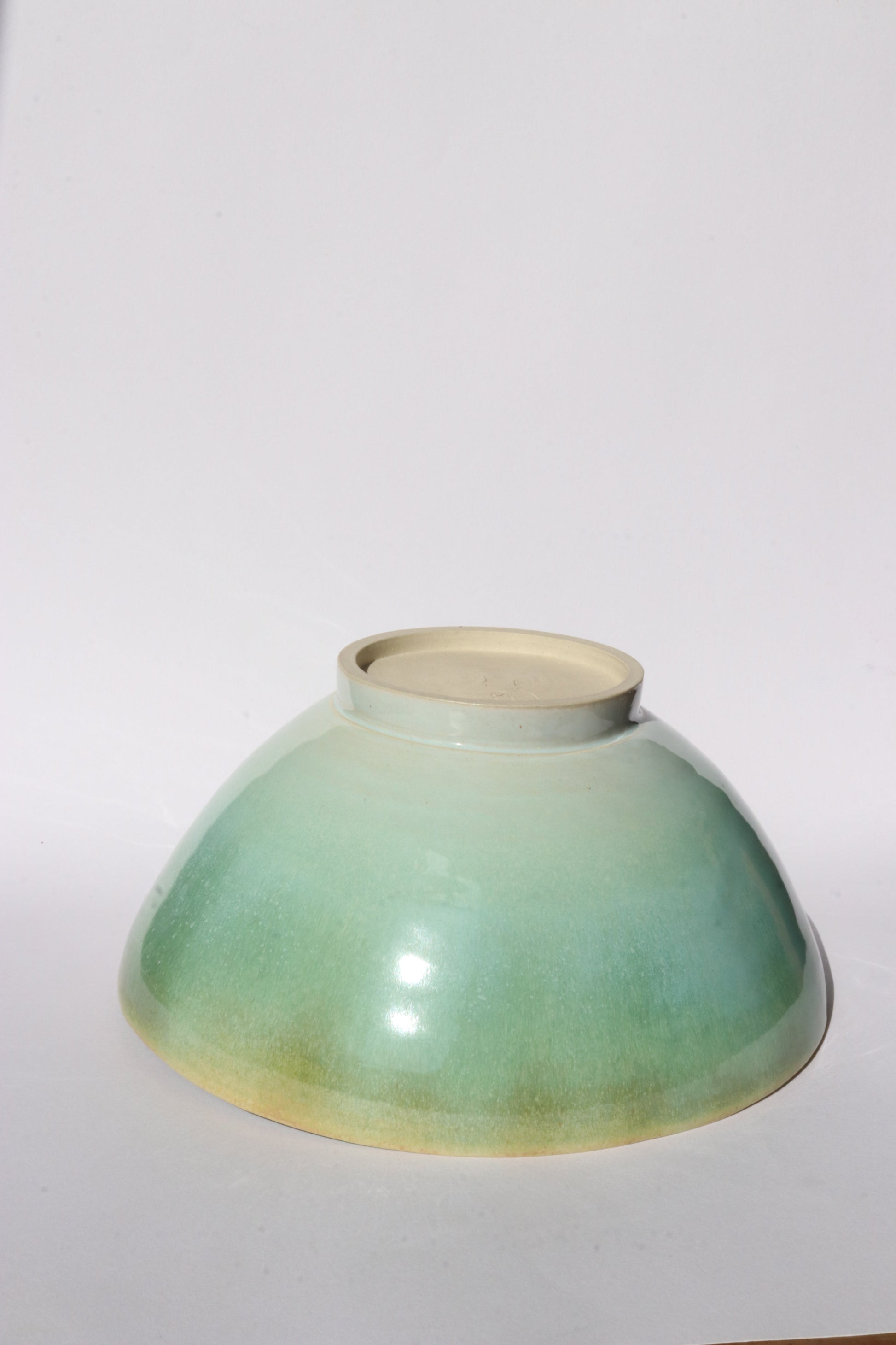 Ceramic bowl turned upside down with greenish-blue glaze on a white background