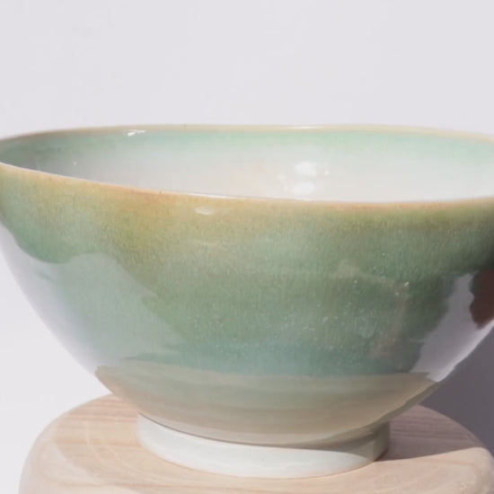 ceramic green bowl slowly turning on itself against white background
