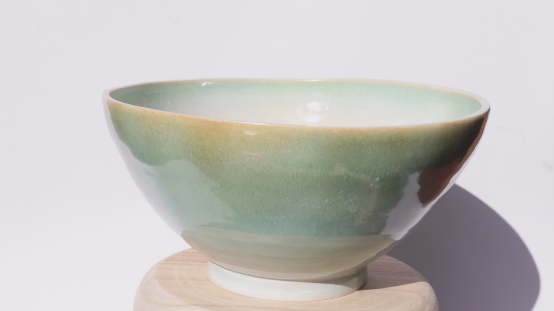 ceramic green bowl slowly turning on itself against white background